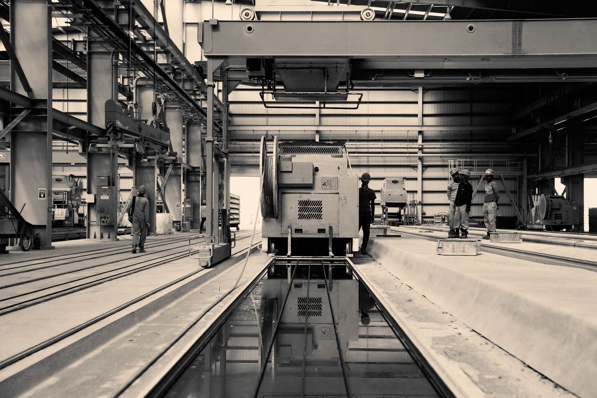 Warehouse / plant interior — cranes, tracks, workers and large machinery, sepia tone
