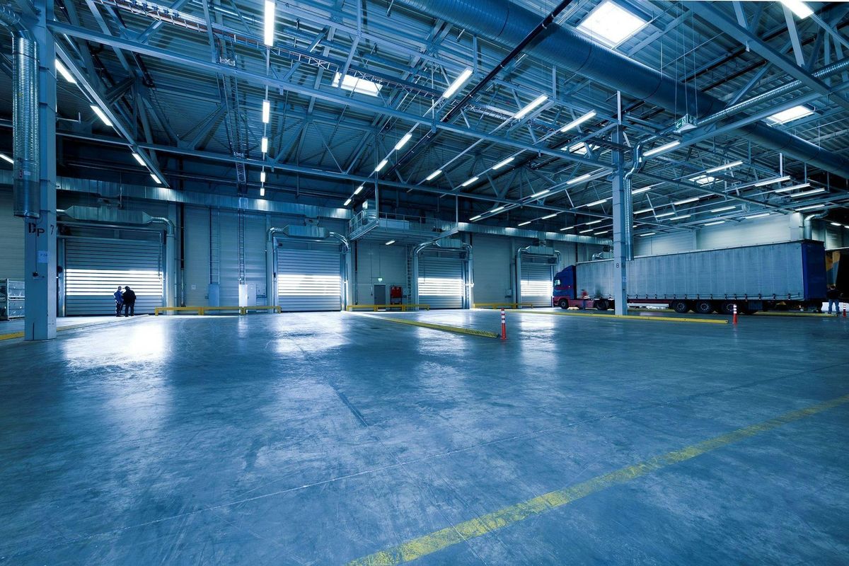 Empty warehouse interior — polished concrete floor, roller doors, truck in the distance, cool blue tone