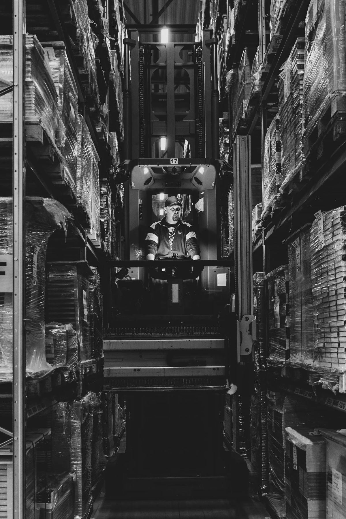 Forklift driver in a warehouse aisle between high racks, black-and-white — Efficient Logistics